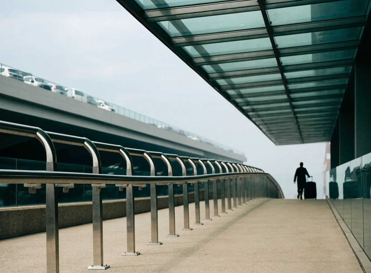 A walkway corridor from a Brisbane Airport car park toward the terminal, with a traveller and a suitcase at mid-distance